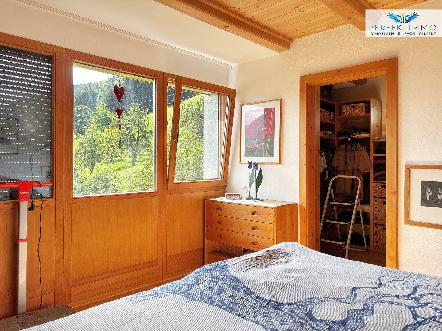 Schlafzimmer mit großen Fenstern, Blick ins Grüne und Zugang zu einem begehbaren Kleiderschrank.