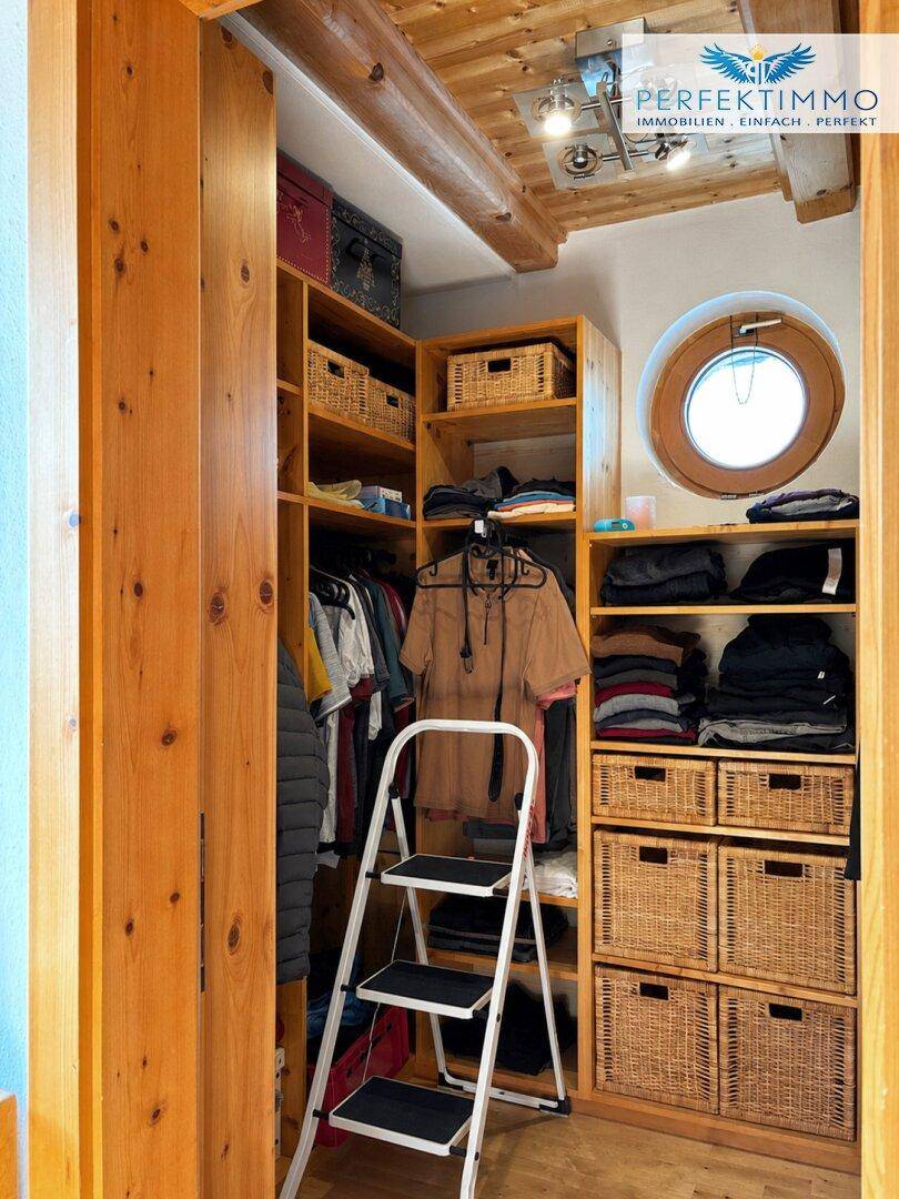 Geräumiger begehbarer Kleiderschrank mit Holzregalen, Körben und runden Fenstern.