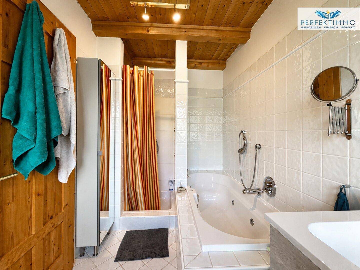 Badezimmer mit Badewanne, Duschvorhang und Waschtisch, weißen Fliesen und Holzbalkendecke.