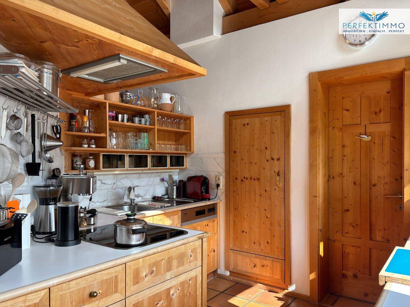 Rustikale Küche mit Holzschränken, Fliesenboden und offener Regalgestaltung unter Holzbalkendecke.