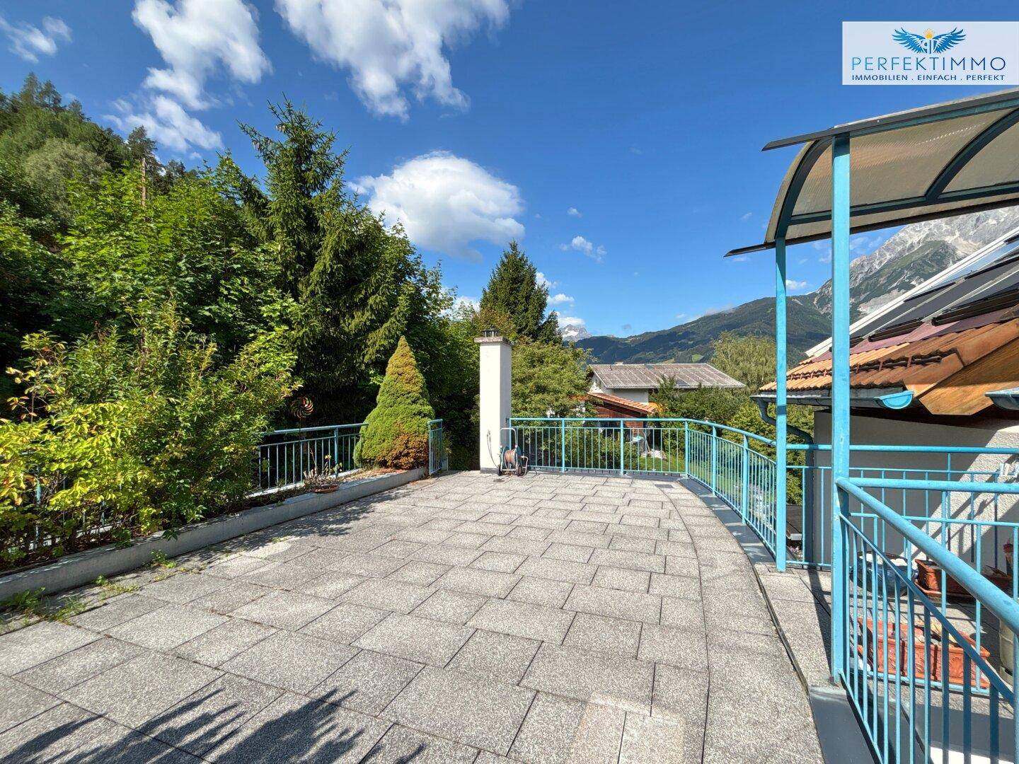 Geräumige Terrasse mit blauer Brüstung und Blick auf die grüne Umgebung und Berge.
