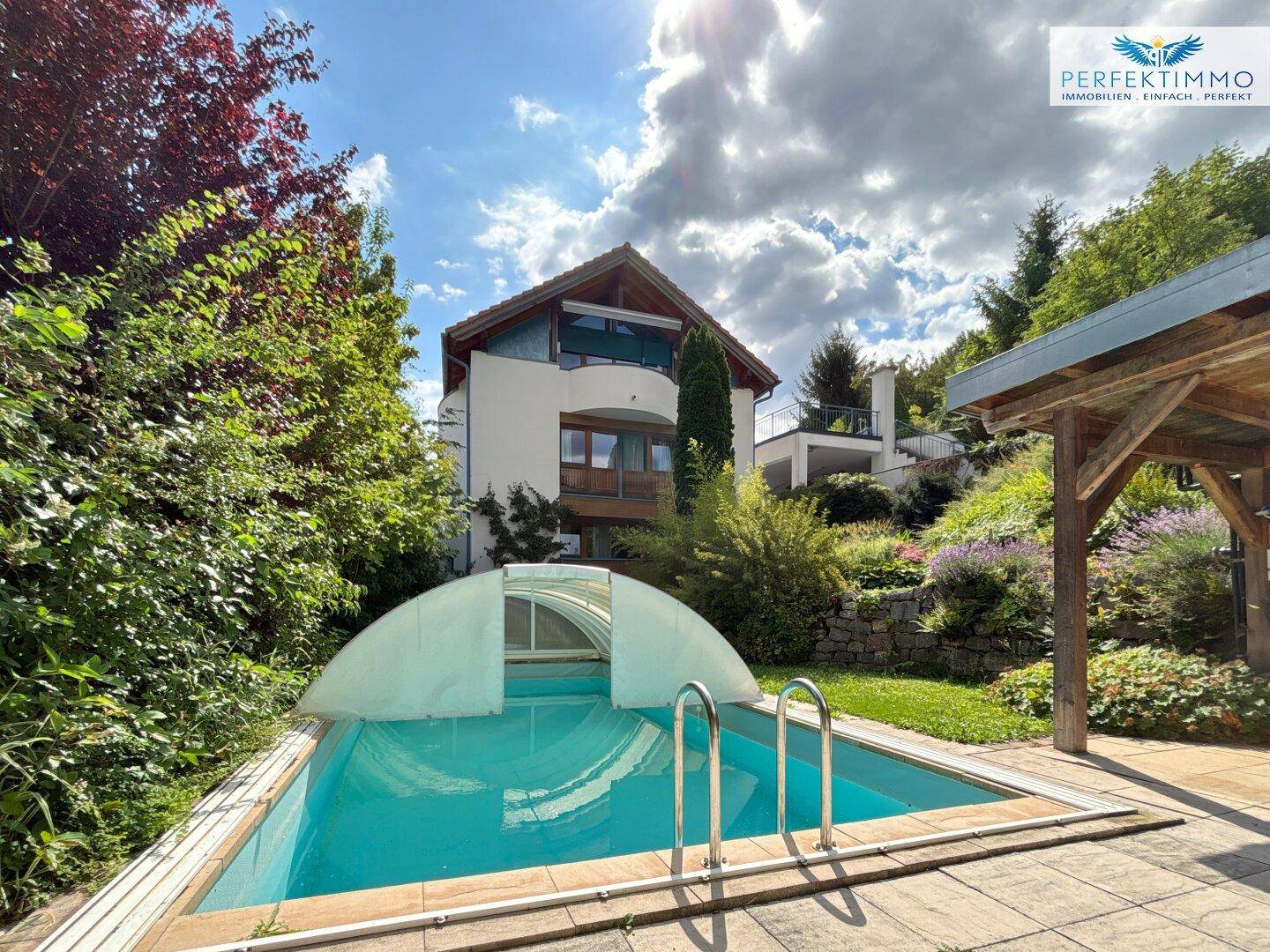 Außenansicht eines Hauses mit Pool und üppigem Garten unter blauem Himmel.