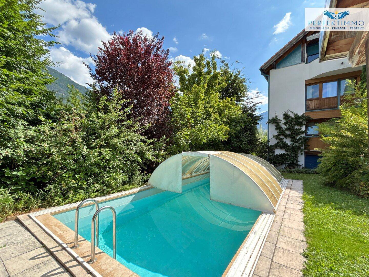 Garten mit Pool und schützender Abdeckung, umgeben von üppiger Vegetation und Bäumen.