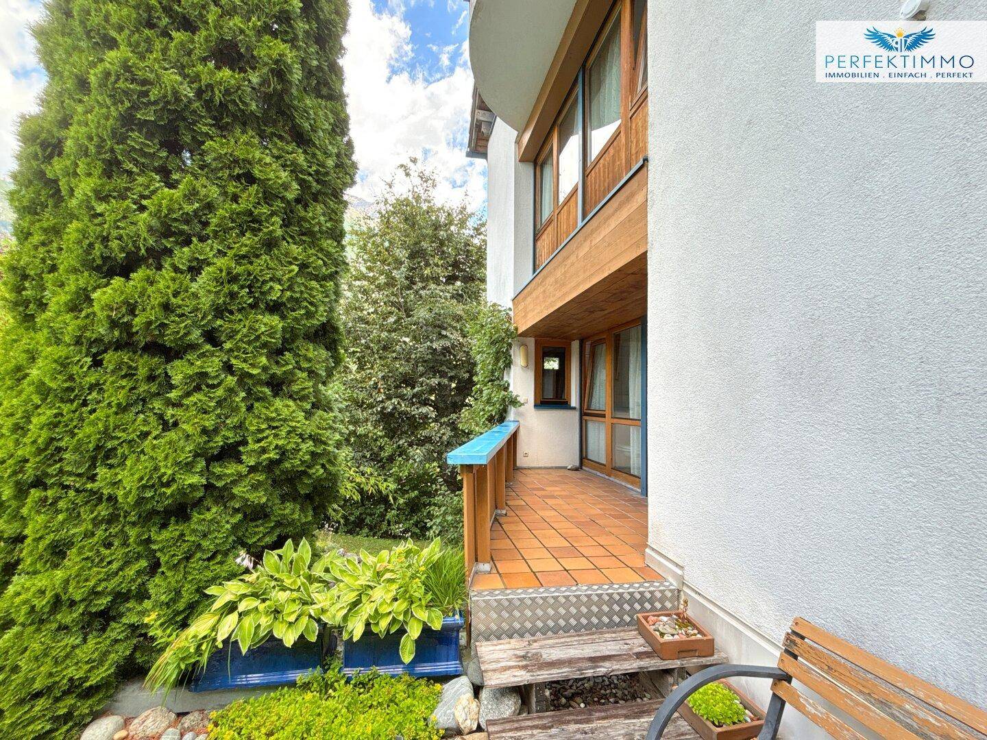 Kleine Terrasse am Haus mit üppiger Bepflanzung und Sitzgelegenheit im Freien.