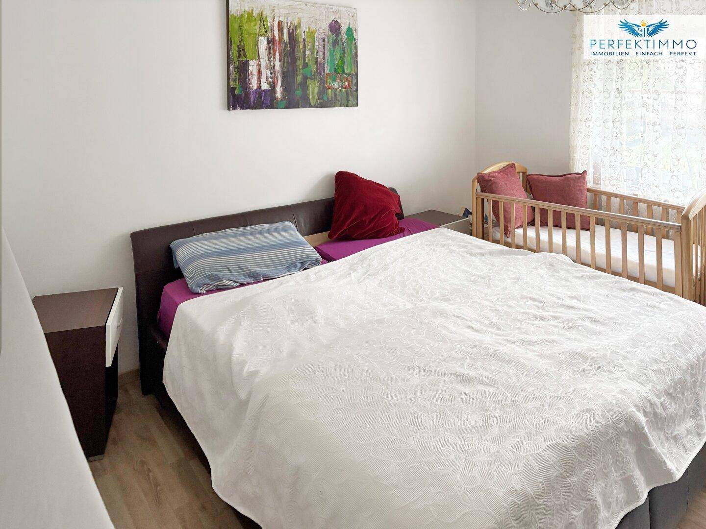 Schlafzimmer mit Doppelbett und Babybett, hell und einfach eingerichtet.
