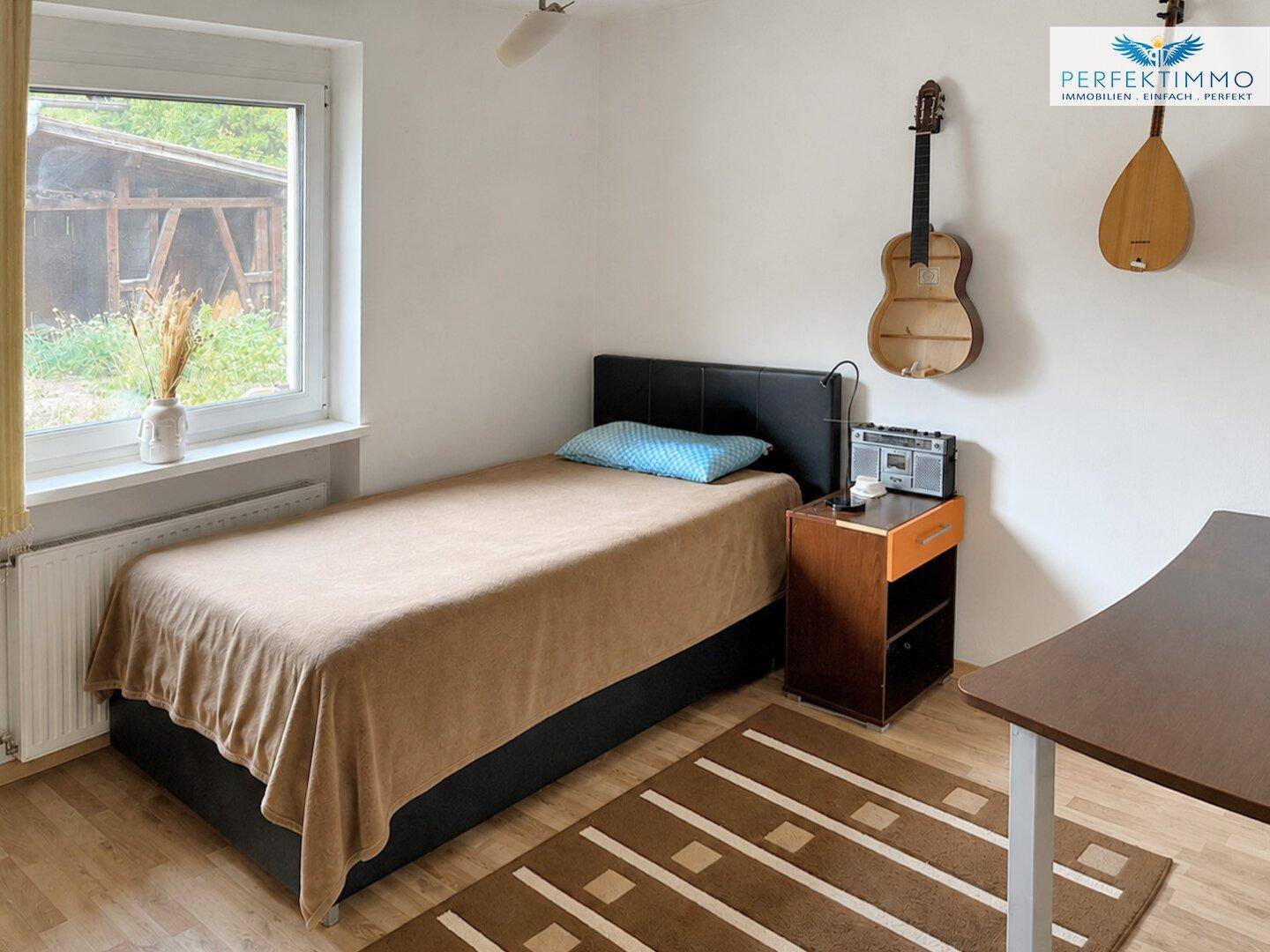 Helles Schlafzimmer mit Einzelbett, Holzboden und Fensterblick ins Grüne.