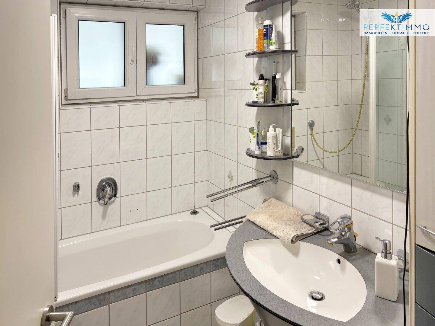 Badezimmer mit Badewanne, Waschbecken und Fenster, weiß gefliest.