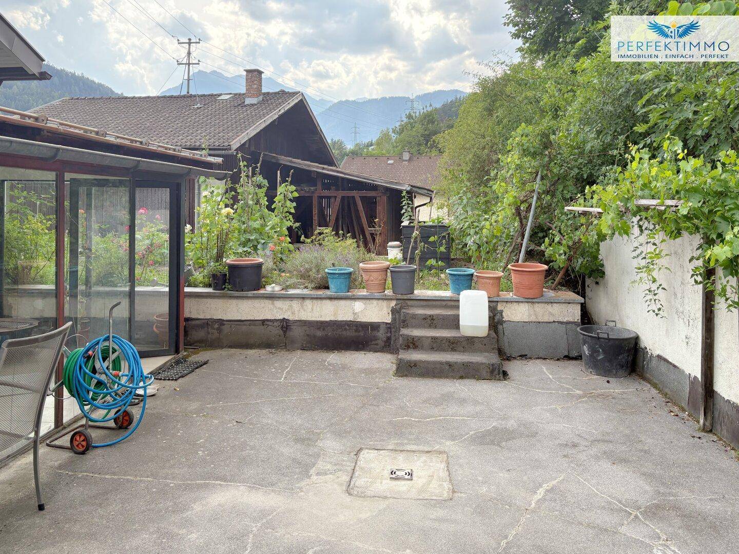 Hinterhof mit gepflastertem Bereich, Pflanzen und Blick auf die Berge.