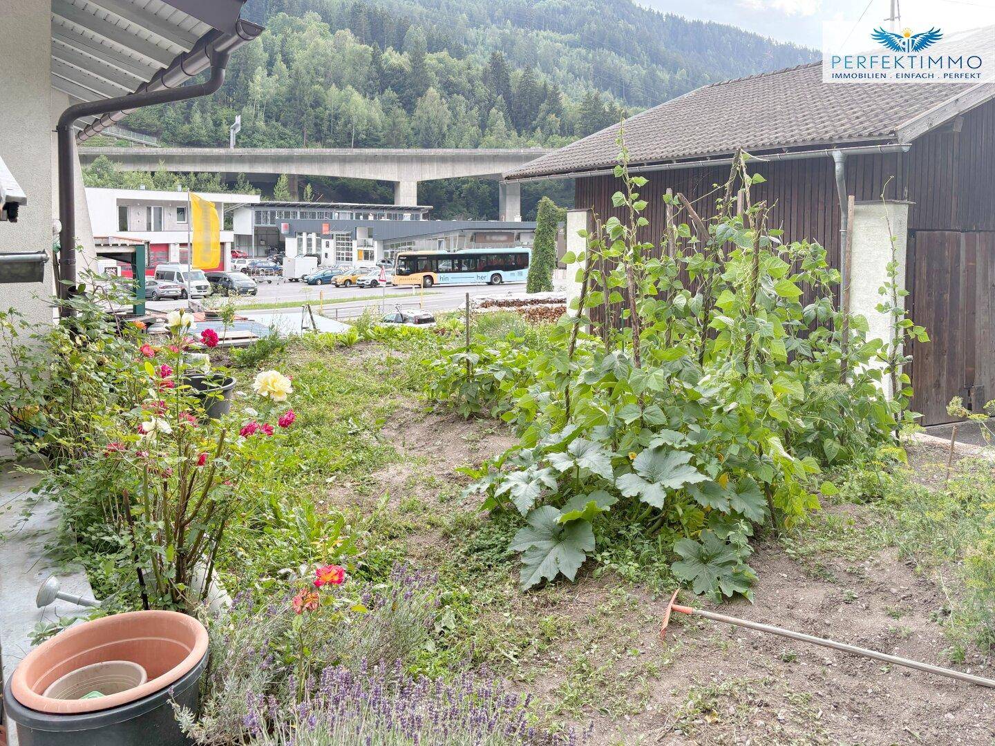 Gartenbereich mit verschiedenen Pflanzen und Blick auf die Straße und Berge.