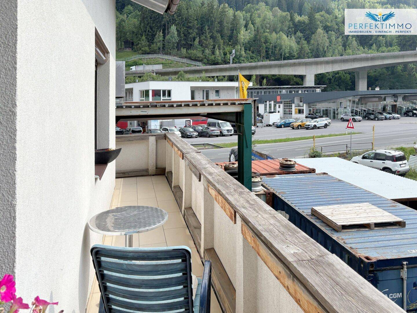 Schmaler Balkon mit Tisch und Stuhl, Blick auf die Straße und Berge.