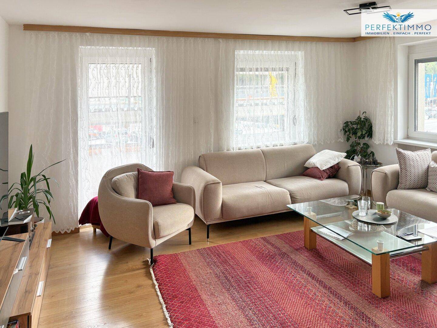 Helles Wohnzimmer mit beigen Sofas, Holzboden und großem Fenster.