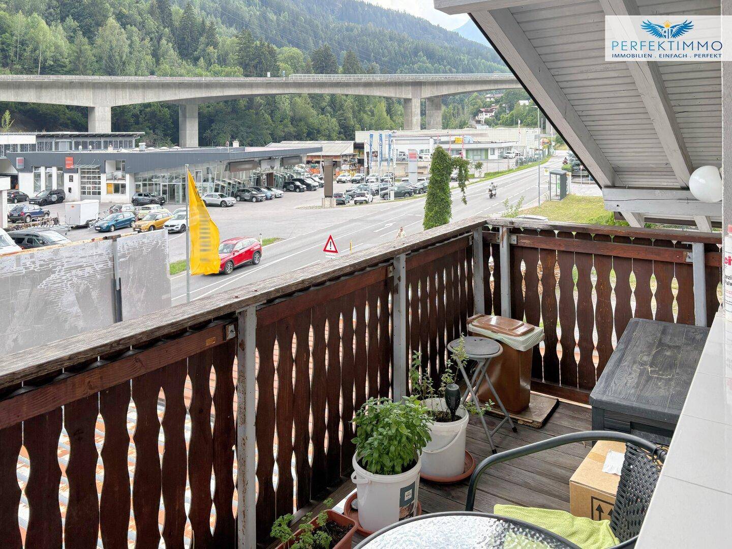 Balkon mit Holzbalken und Blick auf die Straße und die umliegenden Berge.