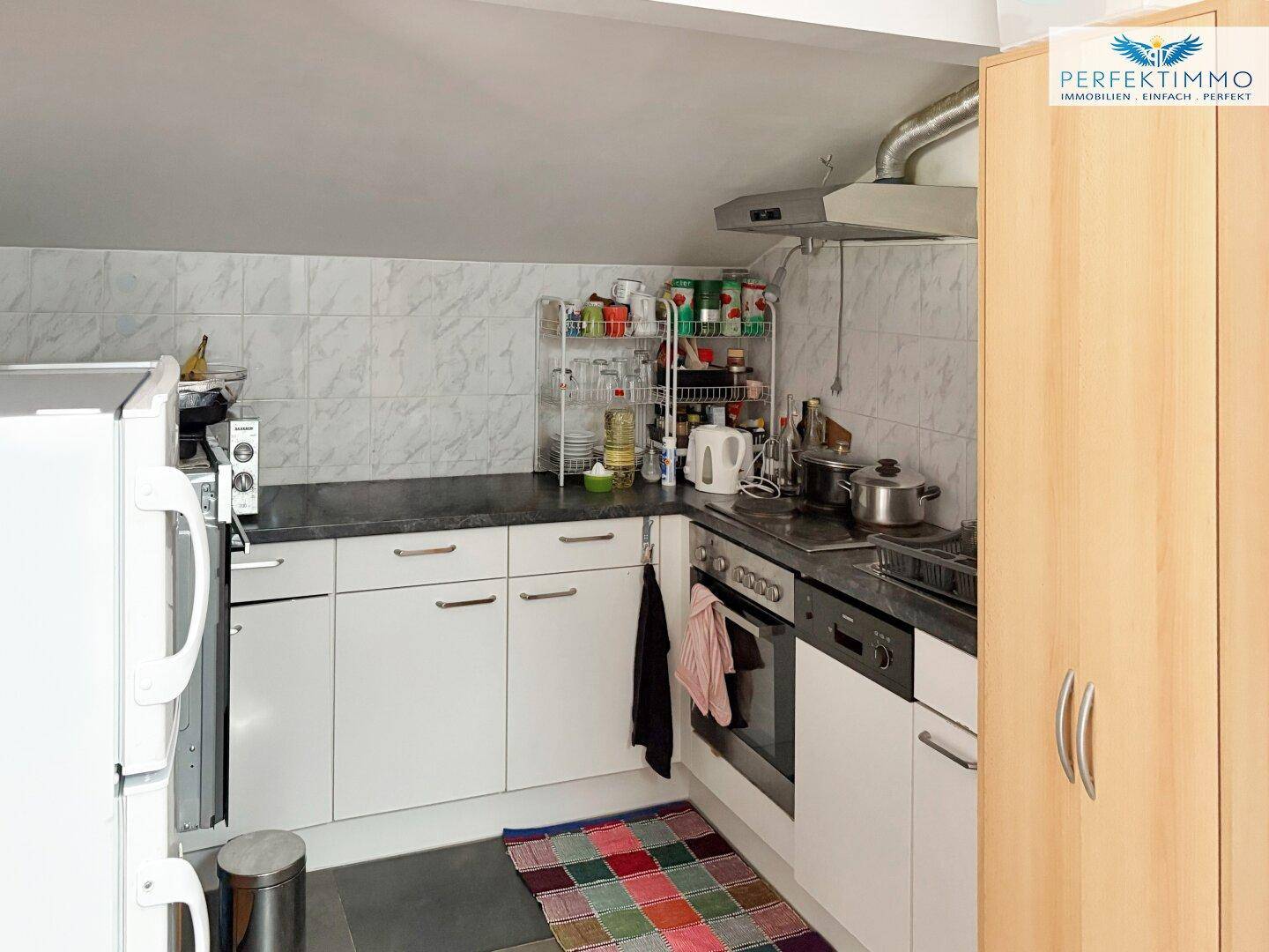 Kleine Küche im Dachgeschoss mit weißen Schränken und Fliesenrückwand.