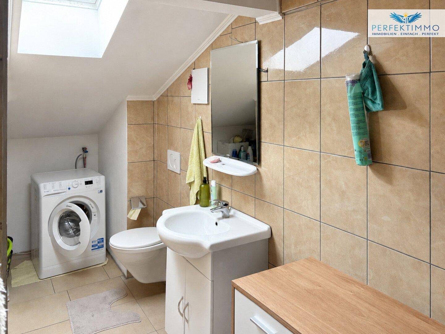 Badezimmer im Dachgeschoss mit Waschmaschine, WC und Dachfenster.