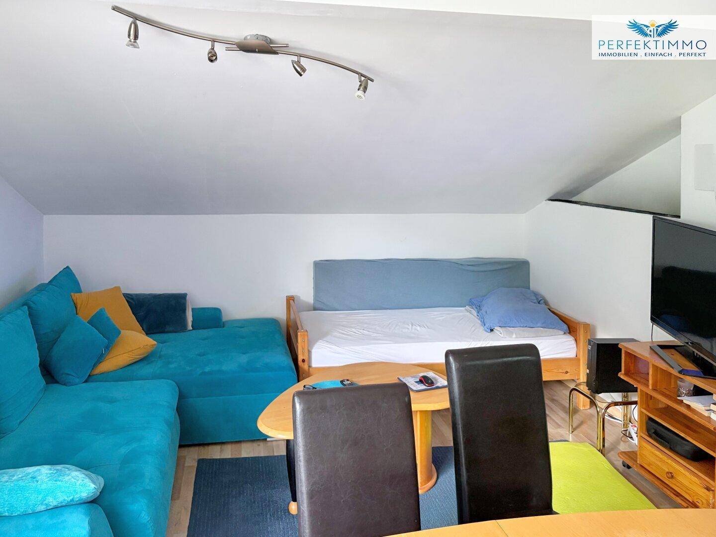 Wohnzimmer im Dachgeschoss mit Sofa, Bett und Esstisch, hell eingerichtet.