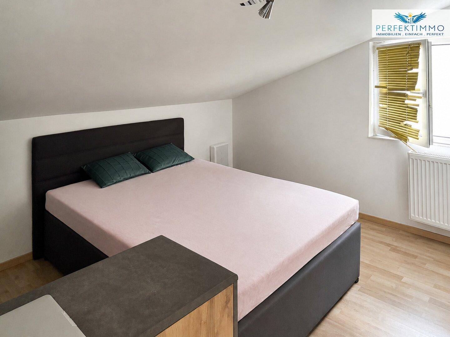 Schlafzimmer im Dachgeschoss mit Doppelbett und Fenster, einfach eingerichtet.