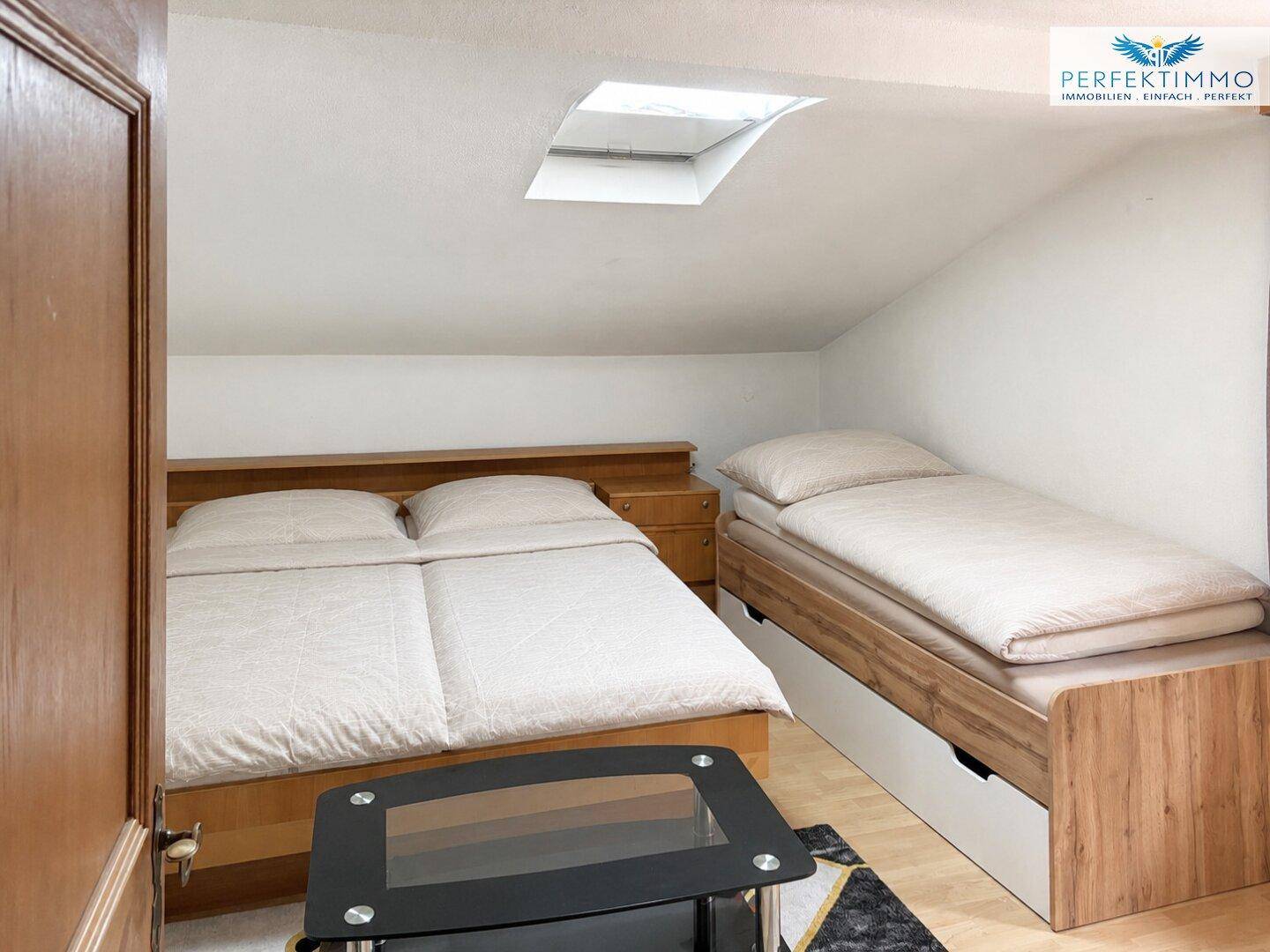 Schlafzimmer im Dachgeschoss mit zwei Betten und Dachfenster.