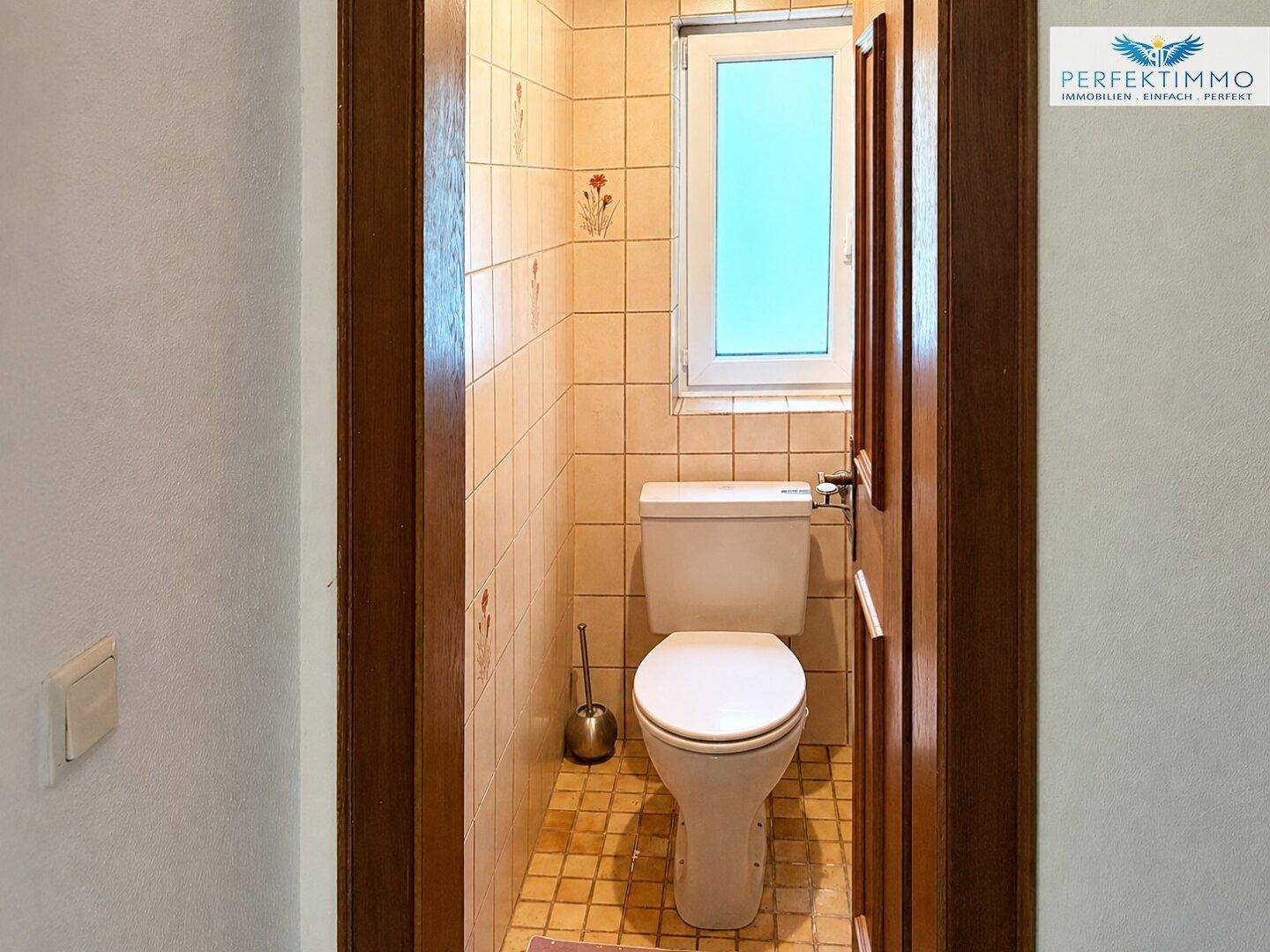 Separate Toilette mit WC und Fenster, beige gefliest.