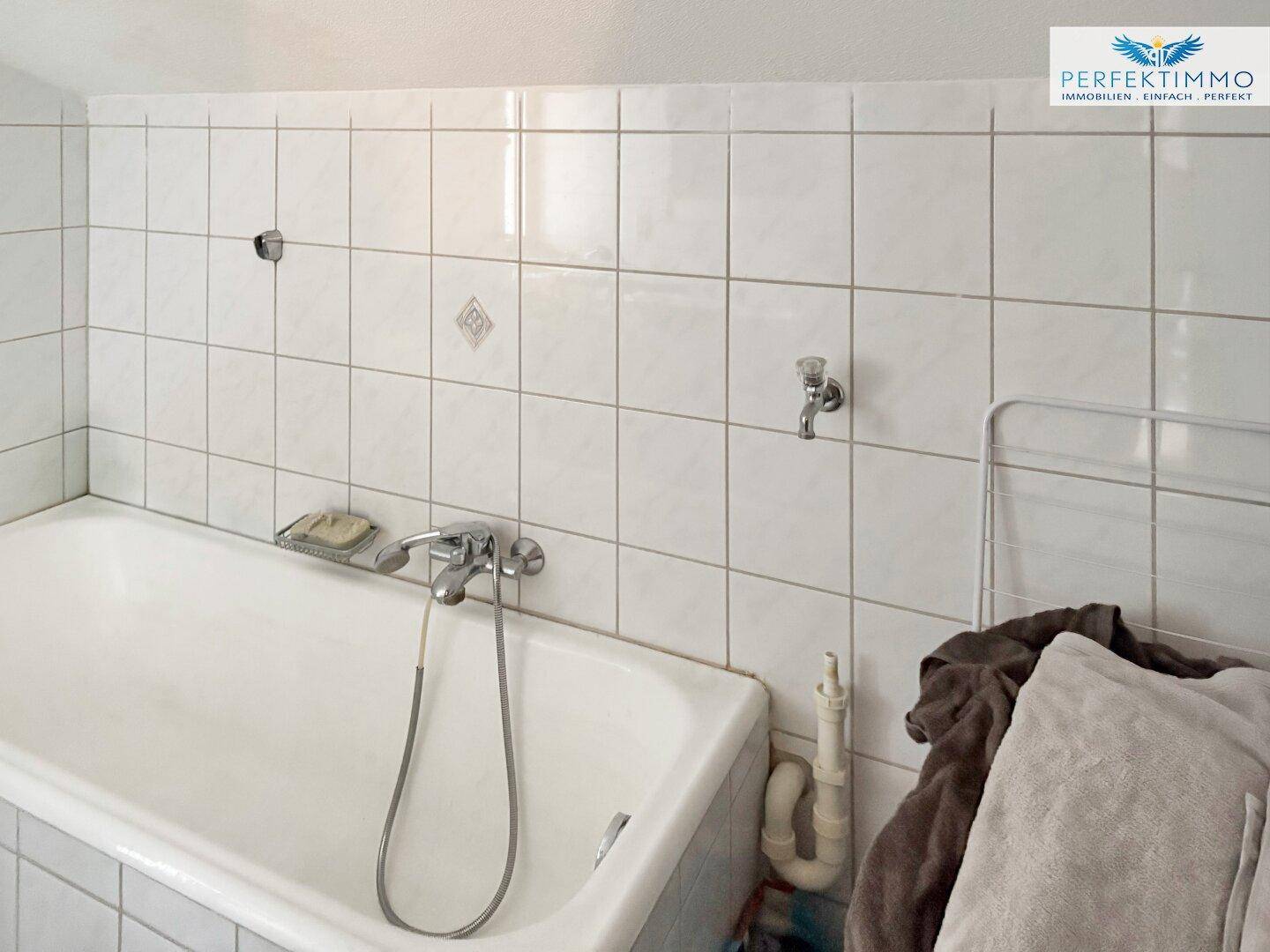Badezimmer mit Badewanne und weißen Fliesen, einfach ausgestattet.
