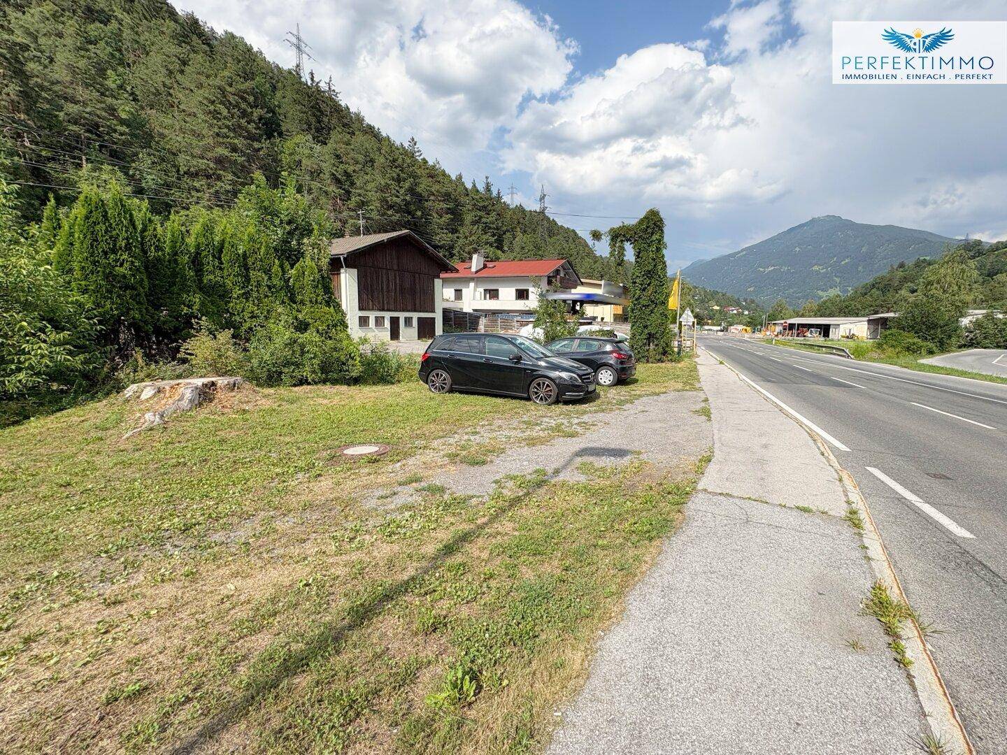 Weitläufiger Außenbereich mit Parkmöglichkeiten, Straße und Bergblick unter bewölktem Himmel.