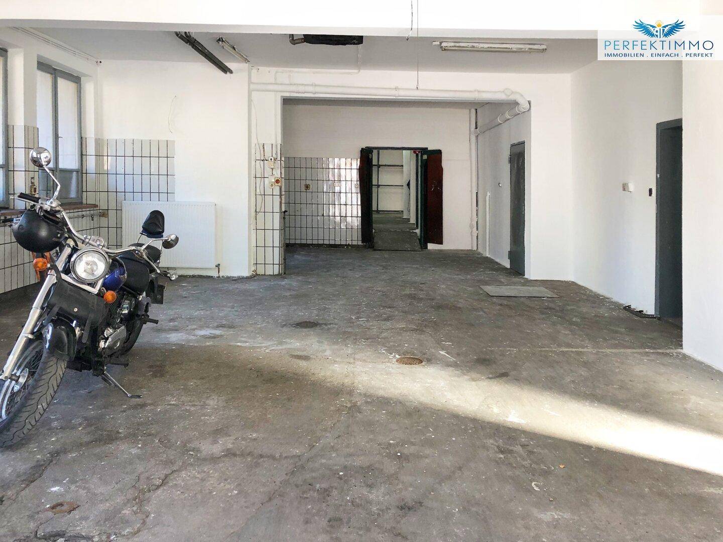 Geräumiger Innenraum mit Betonboden, gefliesten Wänden und einem geparkten Motorrad.