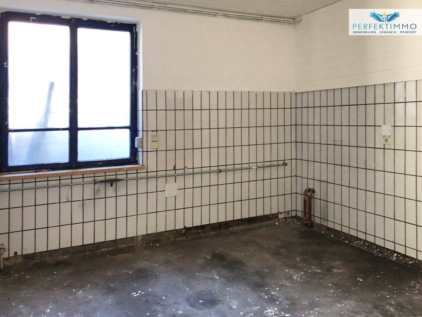 Raum mit gefliesten Wänden, einem Fenster und einem funktionalen, industriellen Charakter.
