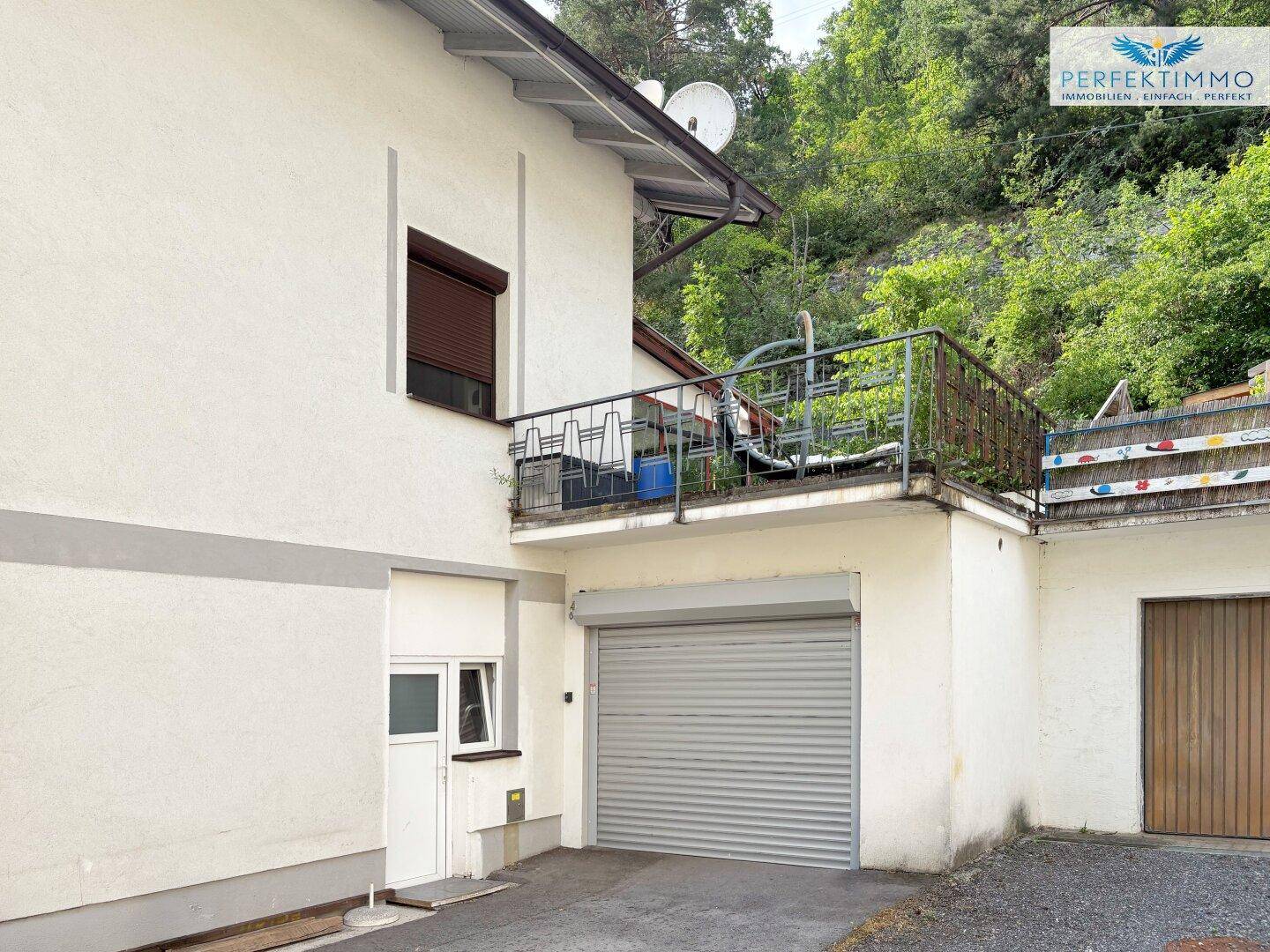 Seitenansicht des Gebäudes mit Garagentor und einem kleinen Balkon mit Metallgeländer.
