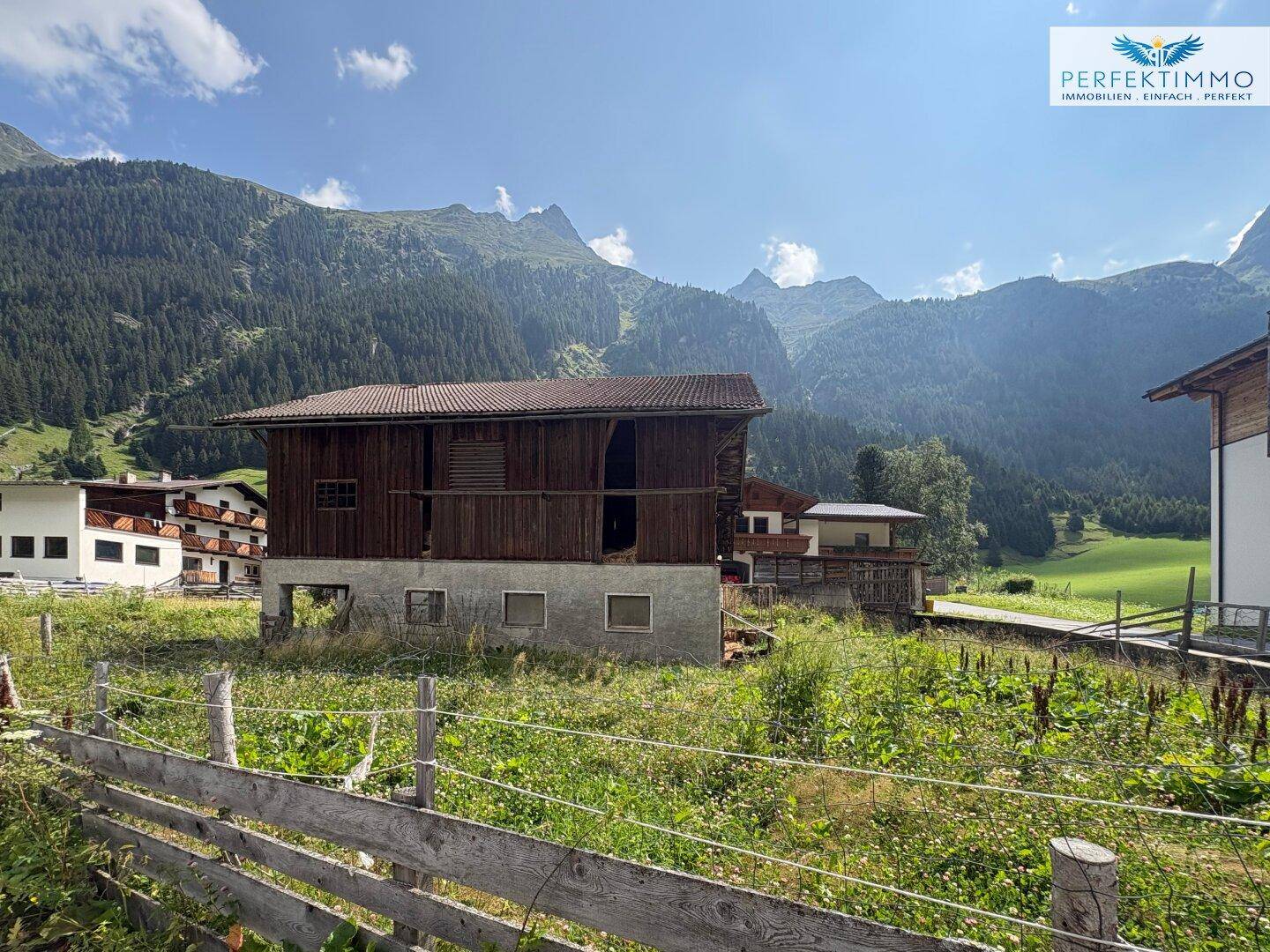 Traditionelles Holzhaus in einer idyllischen Alpenlandschaft, umgeben von Wiesen und hohen Bergen.