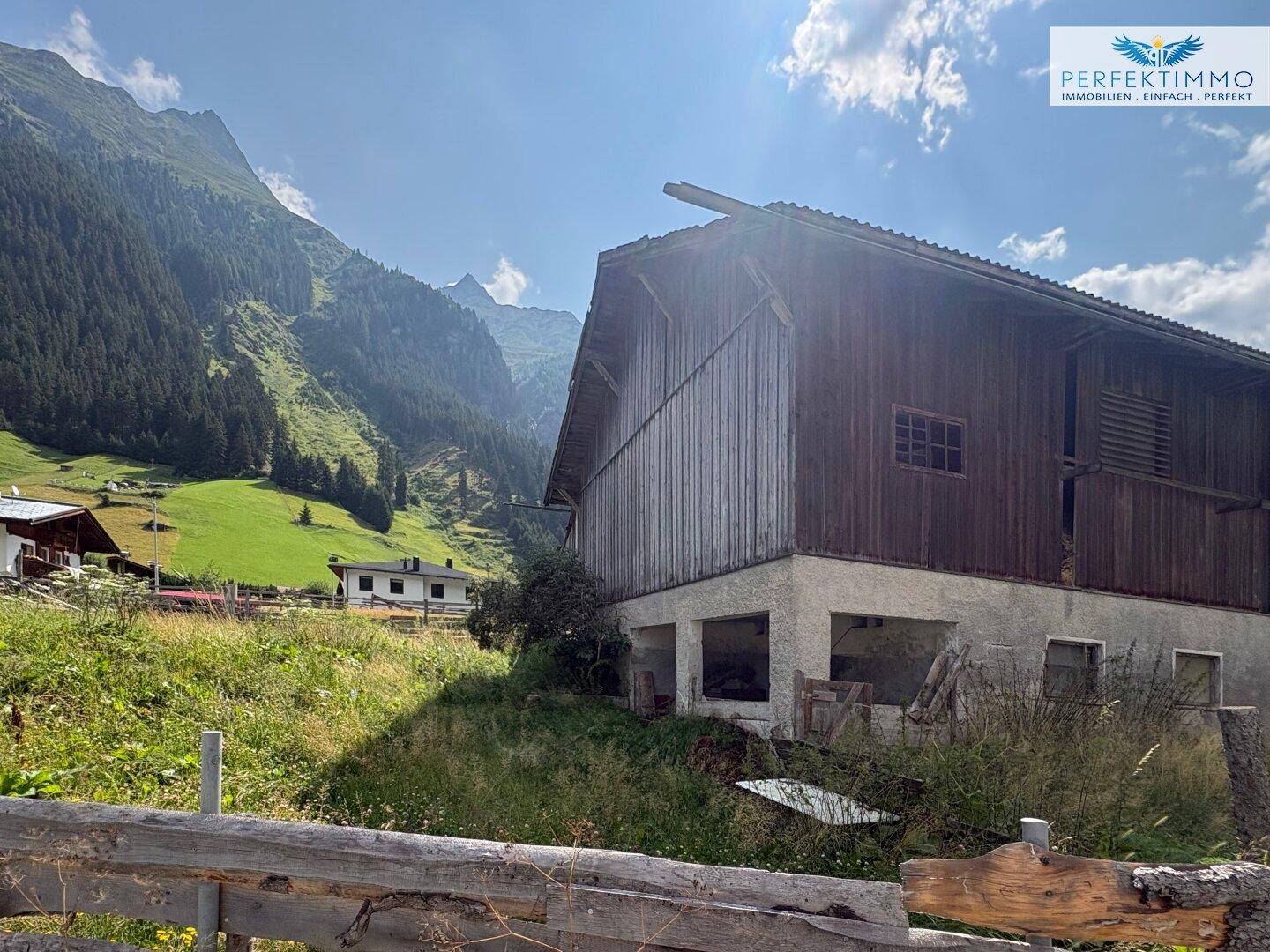 Seitenansicht eines alten Holzgebäudes mit offenem Untergeschoss und Blick auf die Berge.