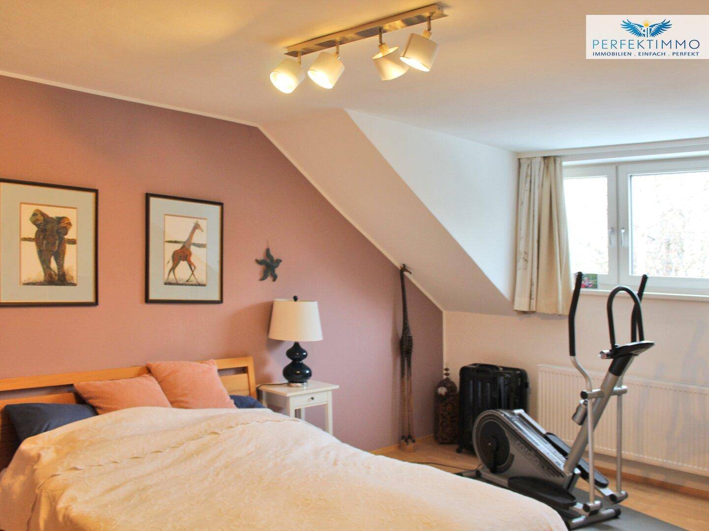 Schlafzimmer im Dachgeschoss mit rosafarbenen Wänden, Holzbett und Fitnessgerät.