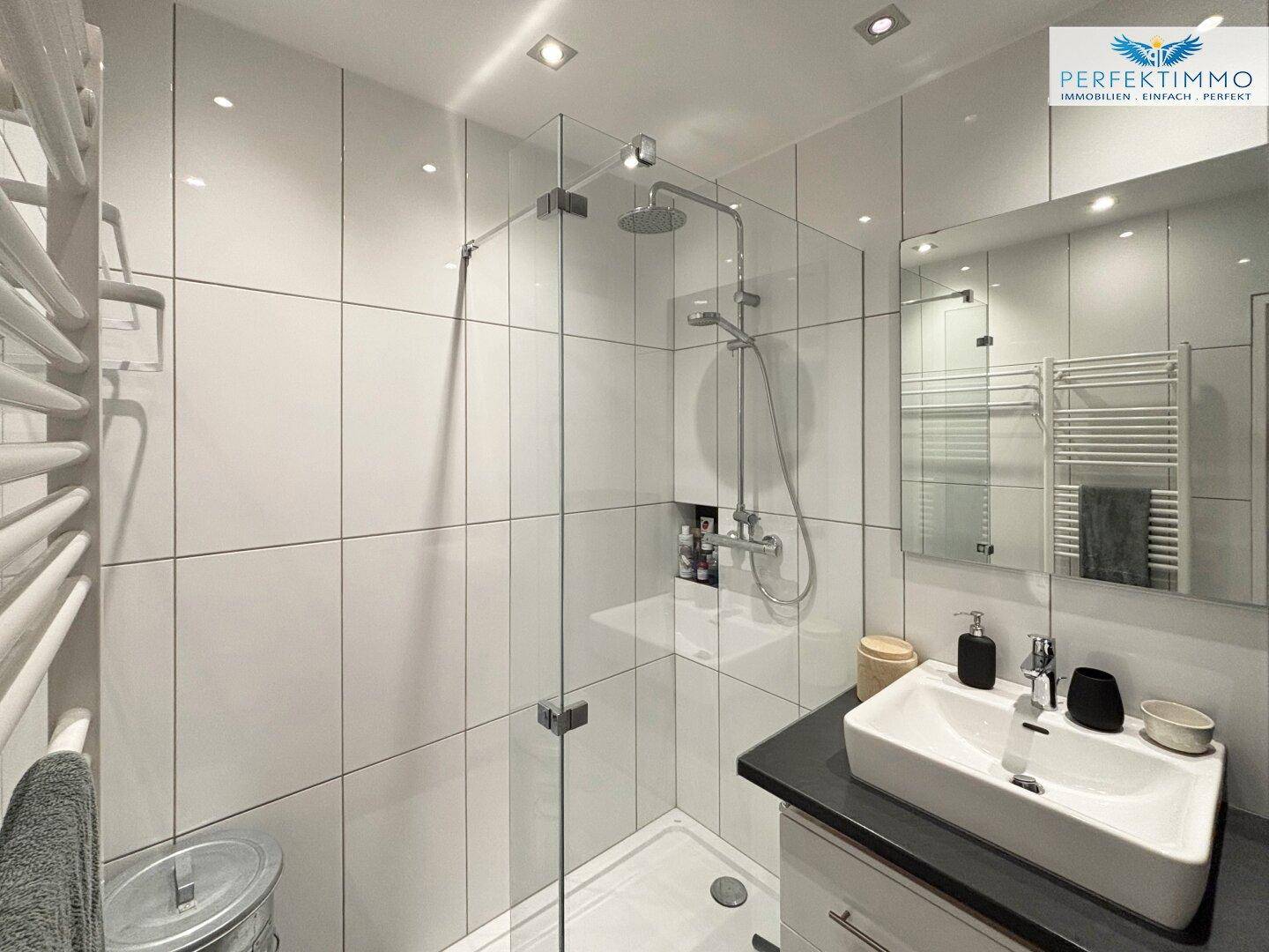 Modernes Badezimmer mit großer begehbarer Dusche, weißen Fliesen und beheiztem Handtuchhalter.