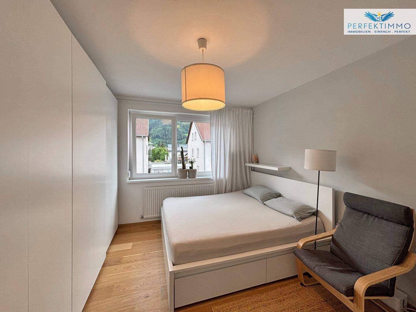 Helles Schlafzimmer mit Holzboden, Doppelbett und Blick auf die umliegende Landschaft.
