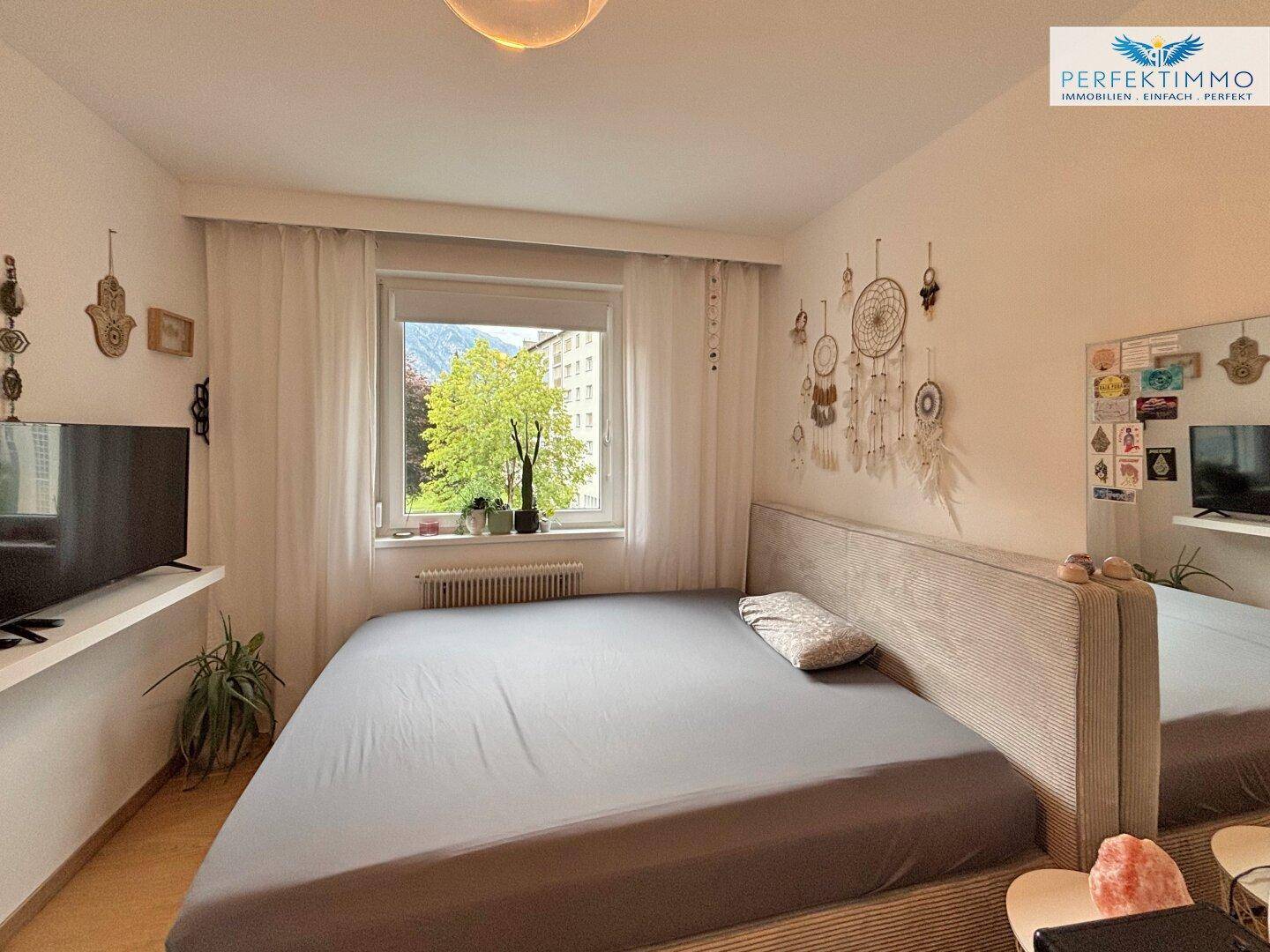 Schlafzimmer mit großem Bett, Fernseher und Blick ins Grüne durch das Fenster.