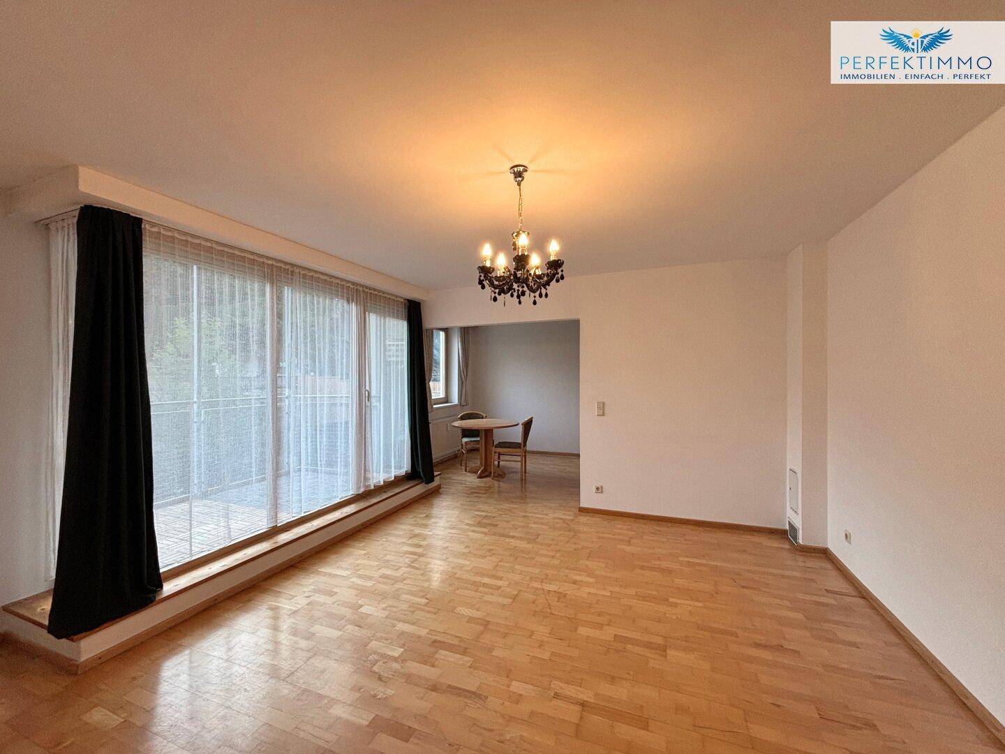 Geräumiger Wohn- und Essbereich mit Parkettboden, großem Fenster und elegantem Kronleuchter.