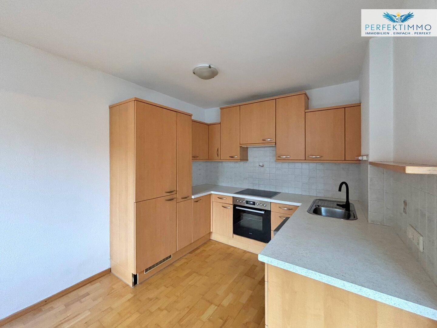 Funktionale Küche mit hellen Holzschränken, integriertem Backofen und weißer Fliesenrückwand.