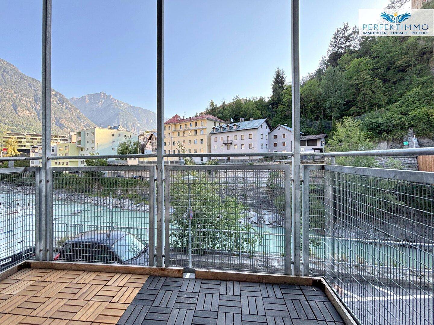 Balkon mit Blick auf den Fluss, umgeben von Bergen und städtischer Bebauung, mit Holzboden.