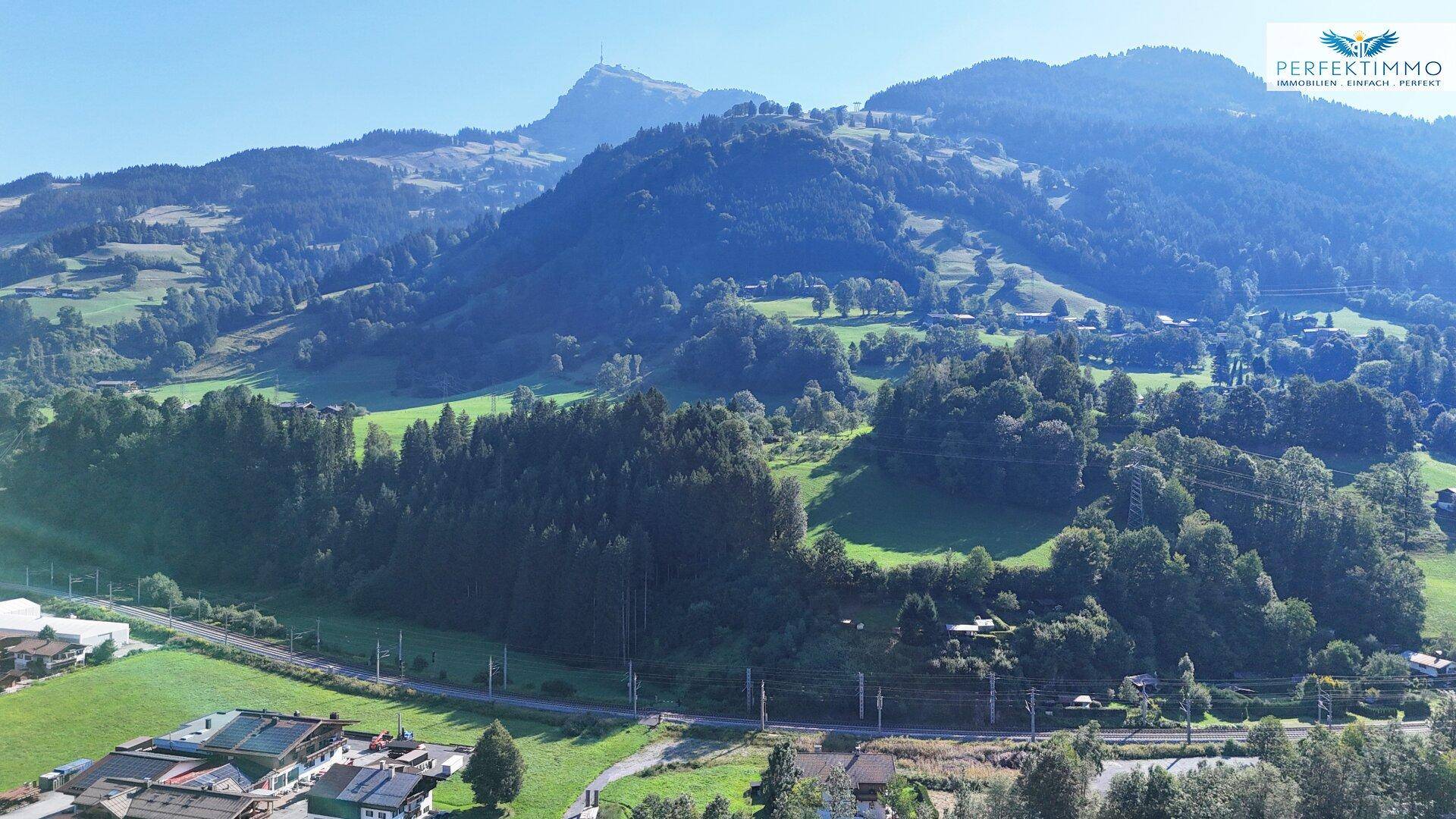 Weitläufige Landschaftsaufnahme mit grünen Hügeln, Wäldern und einem klaren blauen Himmel.