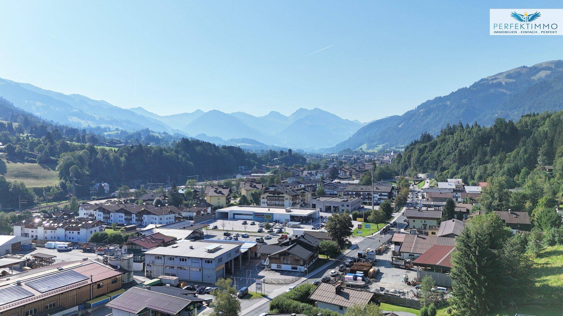 Panoramablick auf eine Stadt im Tal, umgeben von majestätischen Bergen unter blauem Himmel.