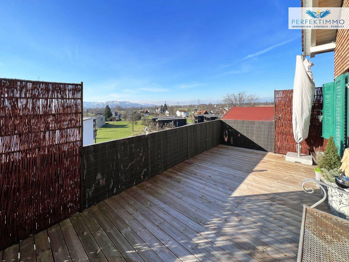 Weitläufige Holzterrasse mit Panoramablick auf die grüne Umgebung und die Dächer der Häuser.