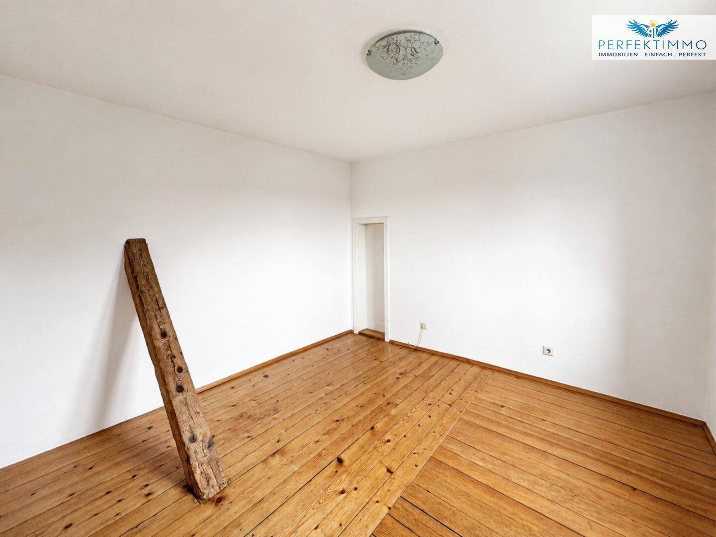 Helles Schlafzimmer mit Holzboden und einem dekorativen Holzbalken, bereit zur individuellen Gestaltung.