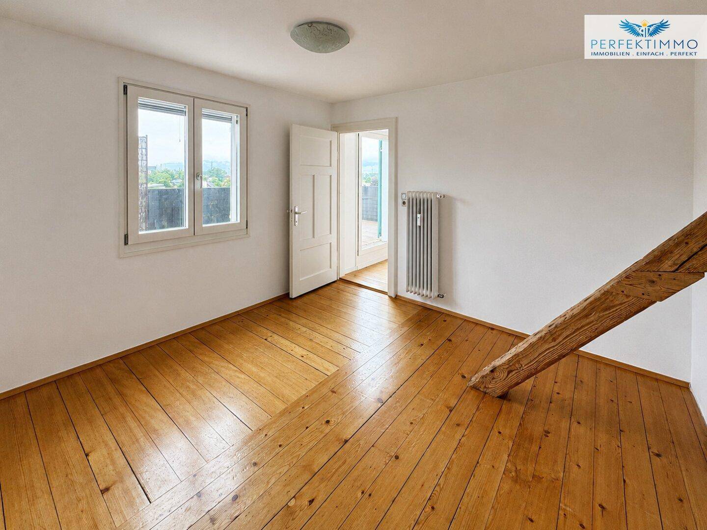 Geräumiges Schlafzimmer mit Holzboden, Fenster und Zugang zu einem weiteren Raum oder Balkon.