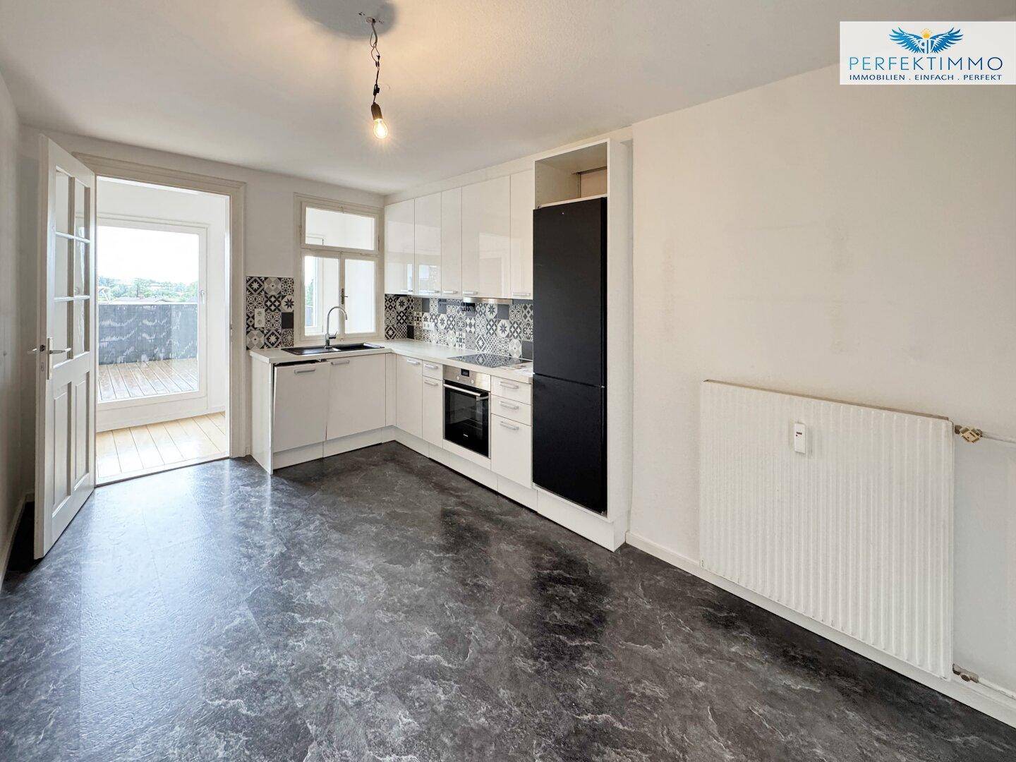 Helle Küche mit Zugang zu einem Balkon, ausgestattet mit modernen weißen Schränken und dunklem Boden.