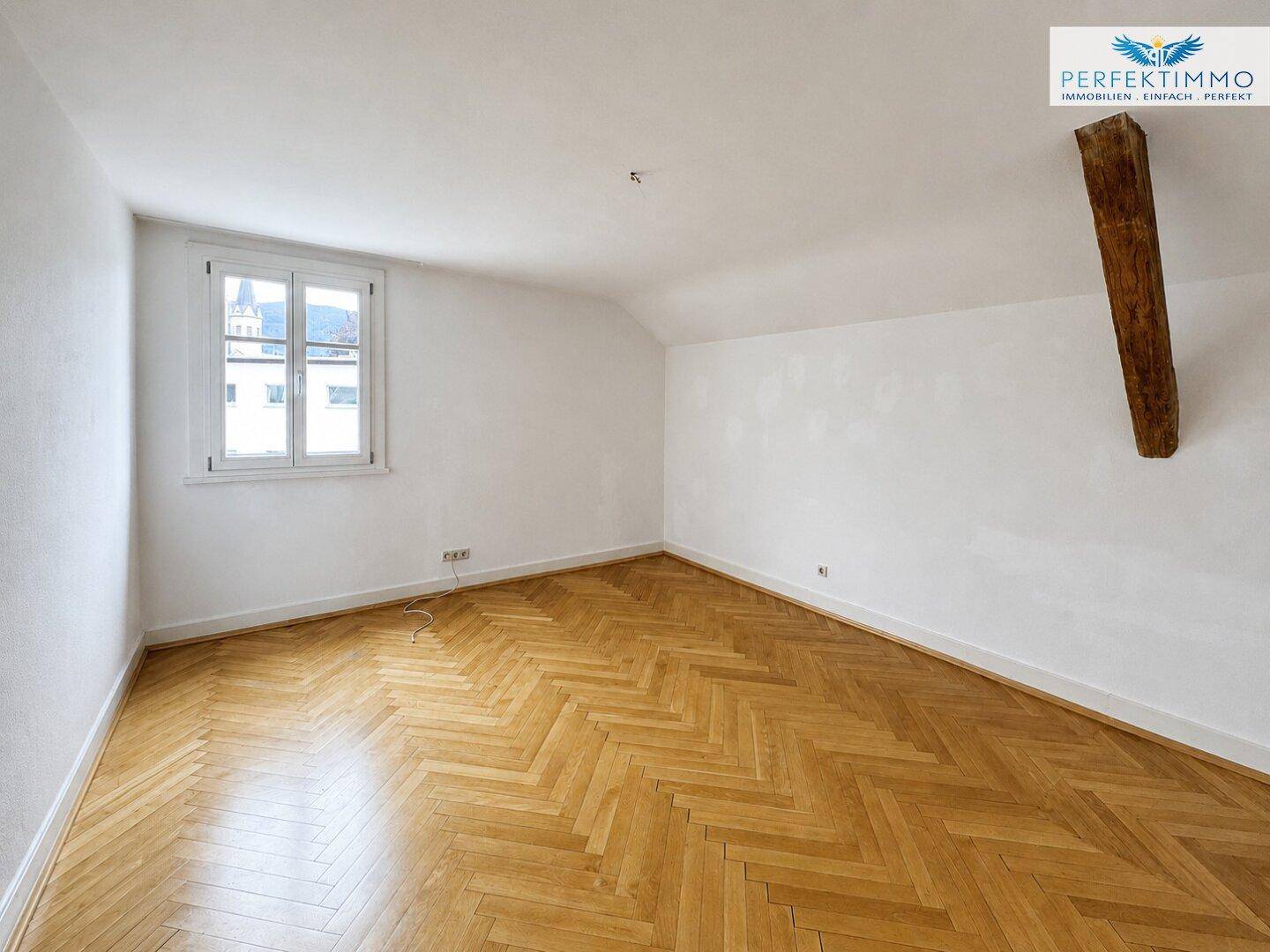 Gemütliches Schlafzimmer mit Fischgrätparkett, Dachschräge und Fenster mit Blick auf die Umgebung.