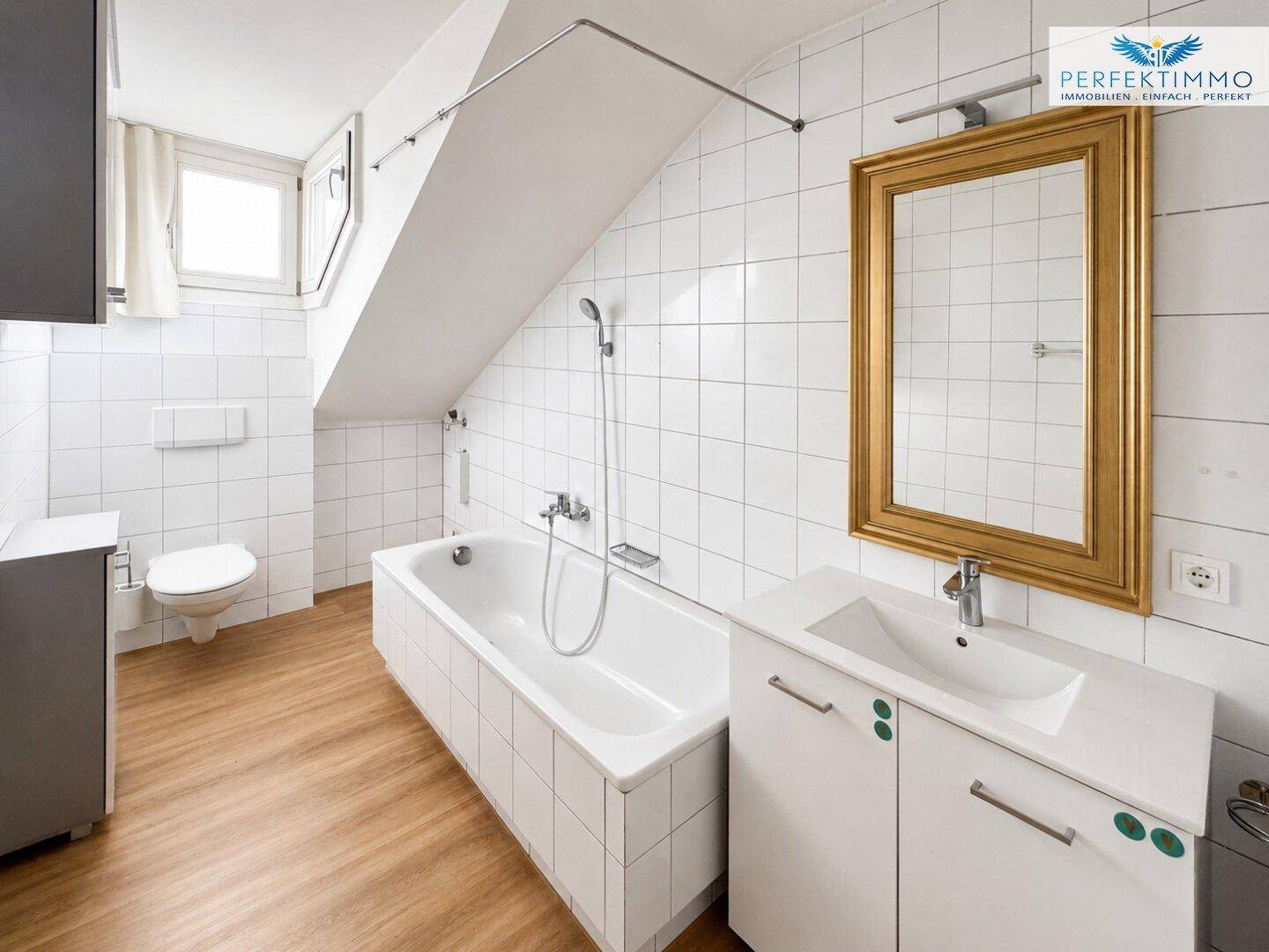 Modernes Badezimmer mit Badewanne, weißen Fliesen und Dachschräge, ausgestattet mit einem Fenster.