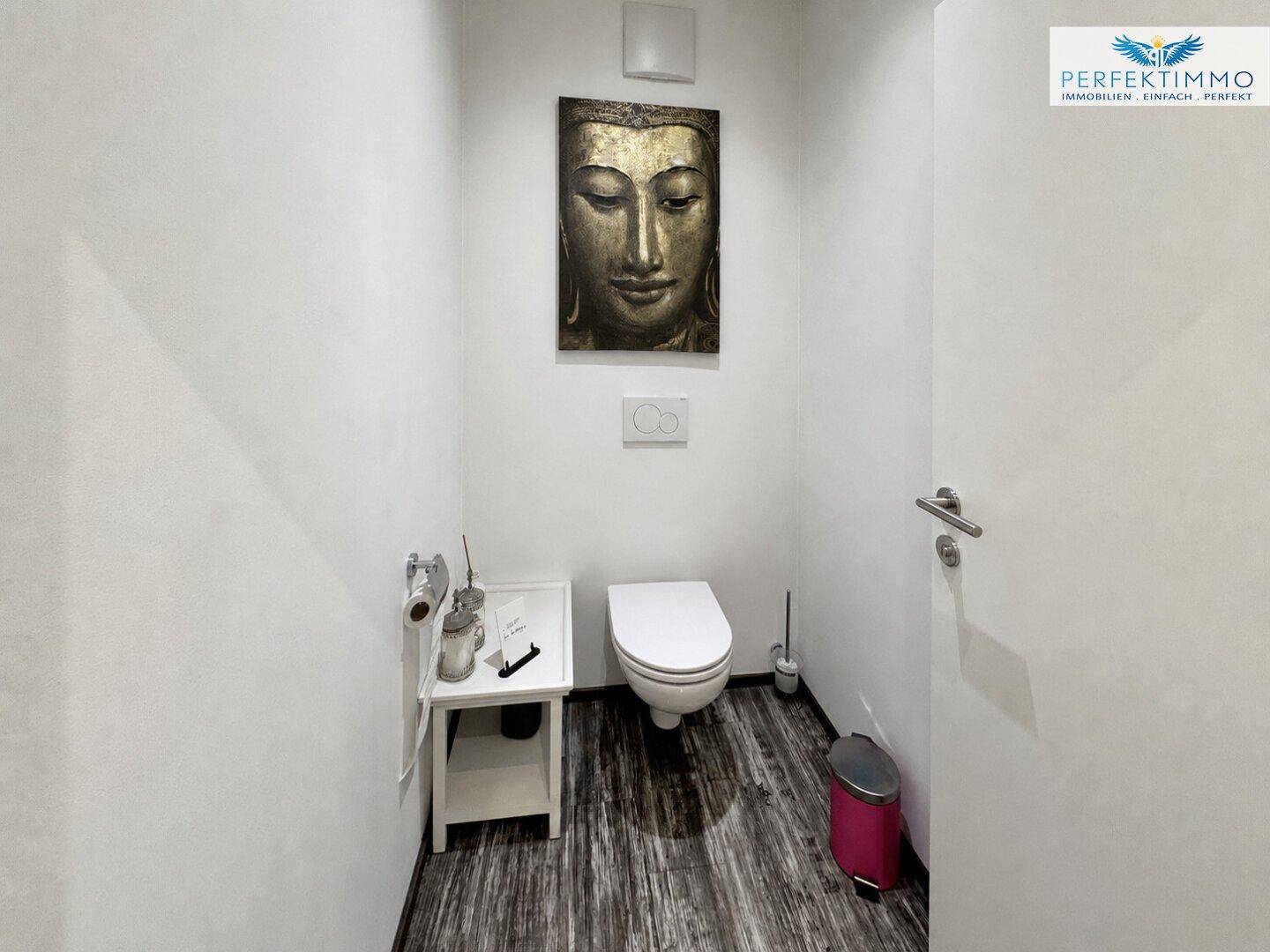 Saubere Toilette mit wandhängendem WC und einem dekorativen Buddha-Wandbild als Akzent.