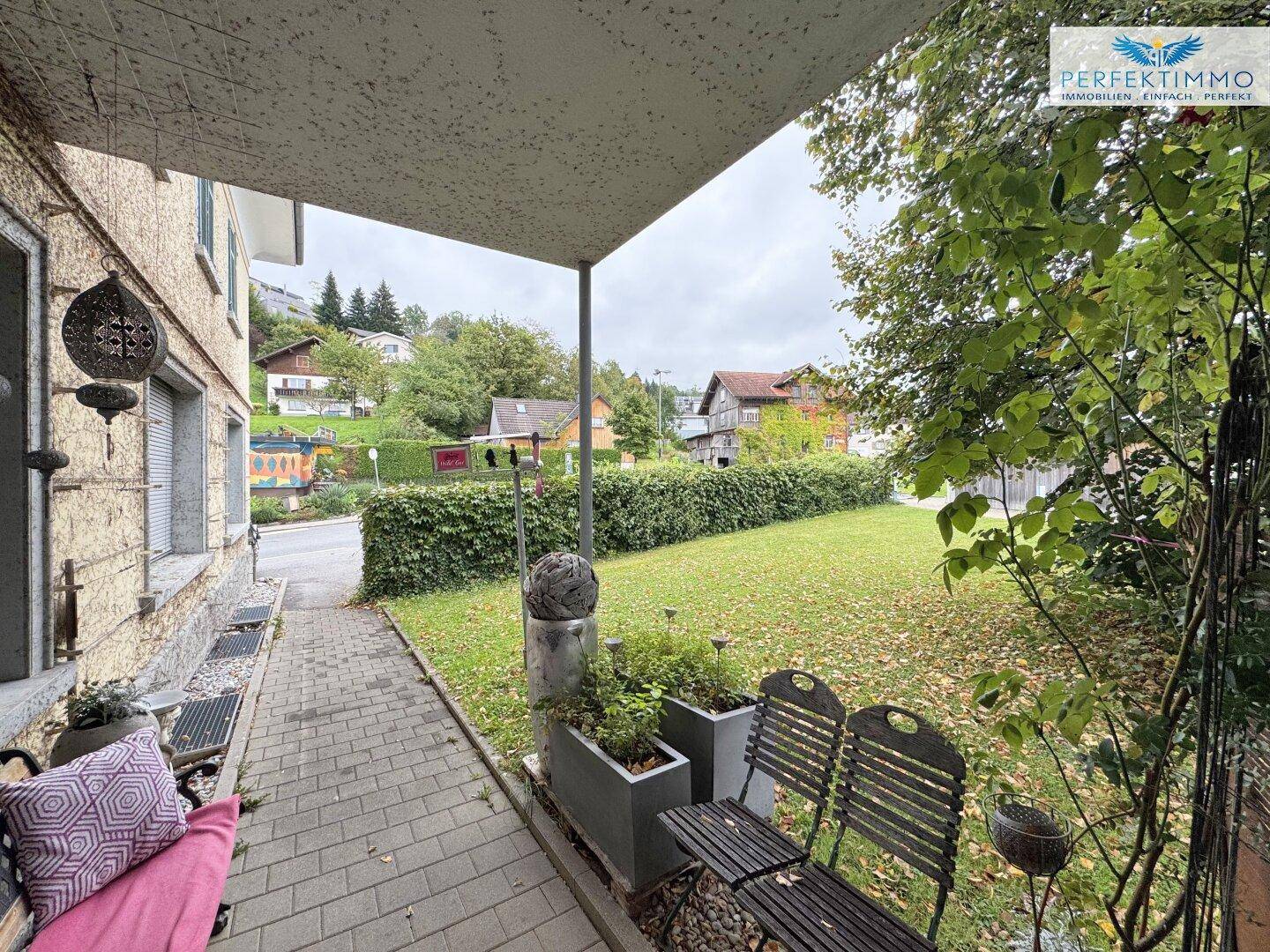 Überdachte Terrasse mit Sitzgelegenheiten und Blick auf den grünen Garten und die umliegende Landschaft.