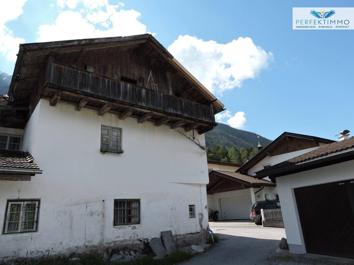 Altes Wohnhaus mit charakteristischem Holzbalkon und angrenzender Garage im Hintergrund.