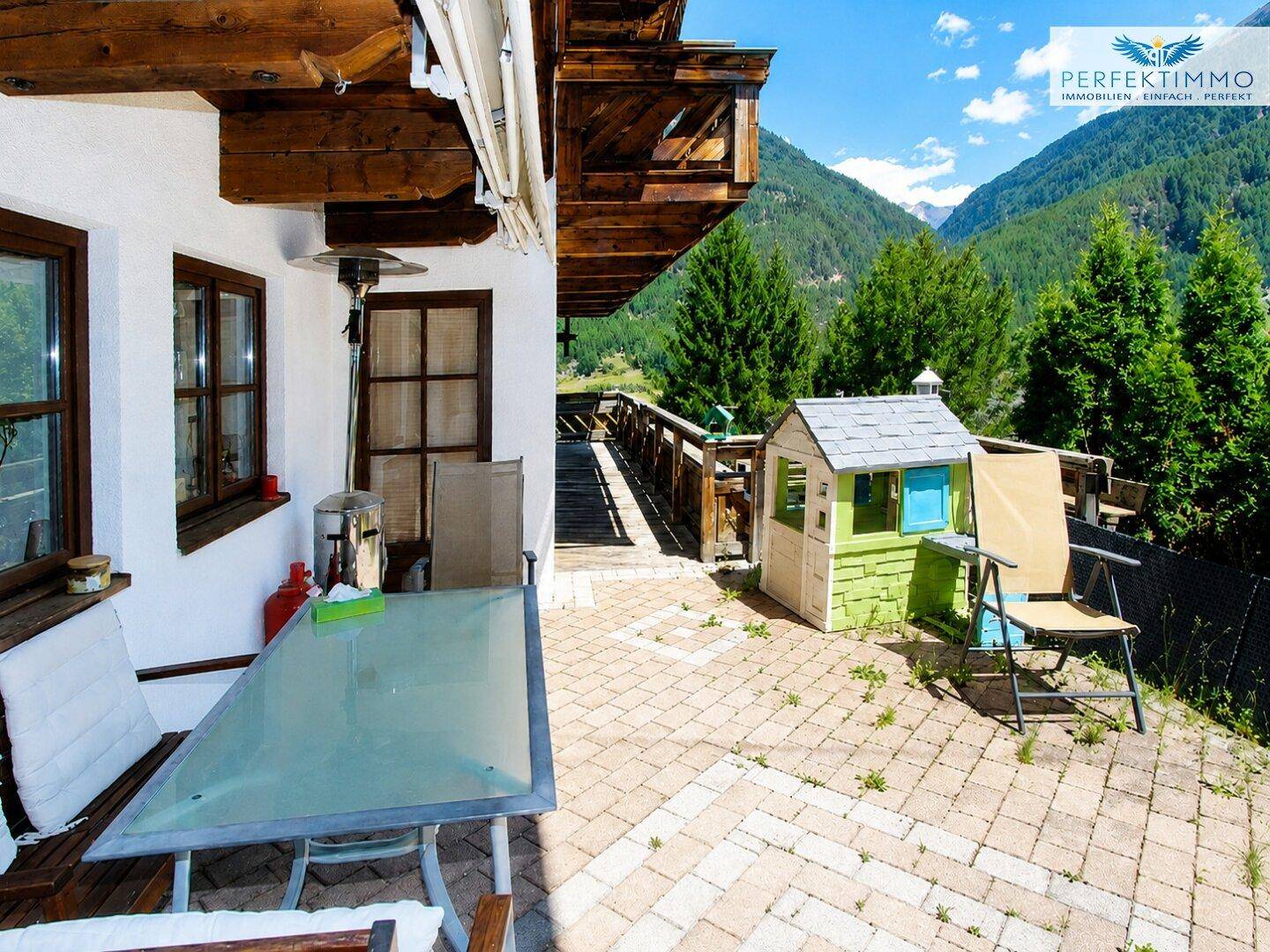 Gemütliche Terrasse mit Sitzgelegenheiten und Spielhaus, umgeben von alpiner Berglandschaft.