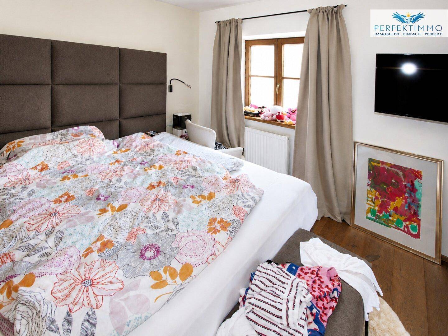 Gemütliches Schlafzimmer mit großem Bett, floraler Bettwäsche und Holzboden.