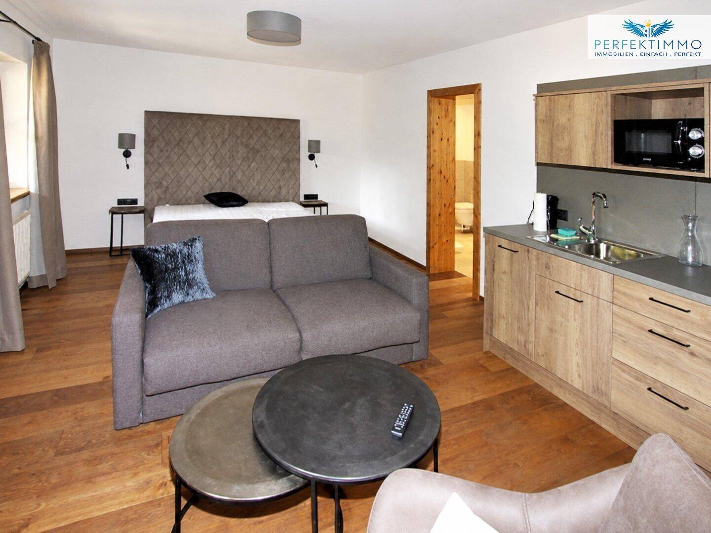 Modernes Wohnzimmer mit Sofa, Couchtisch und integrierter Küchenzeile.